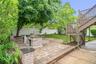 Paved patio area featuring two stone-clad built-in structures, a tiered wooden deck with railings and staircase, and a manicured lawn