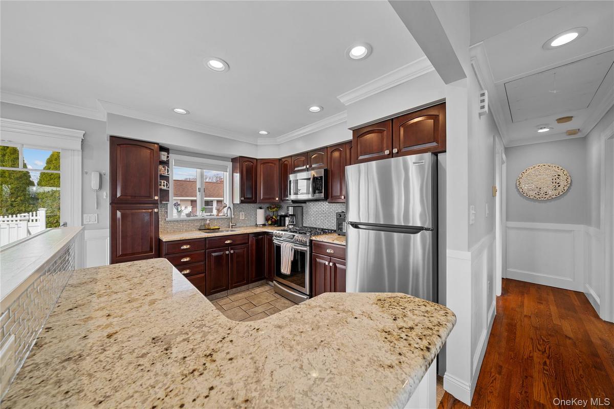 Kitchen featuring a wainscoted wall, stainless steel appliances, light stone counters, backsplash, and ornamental molding