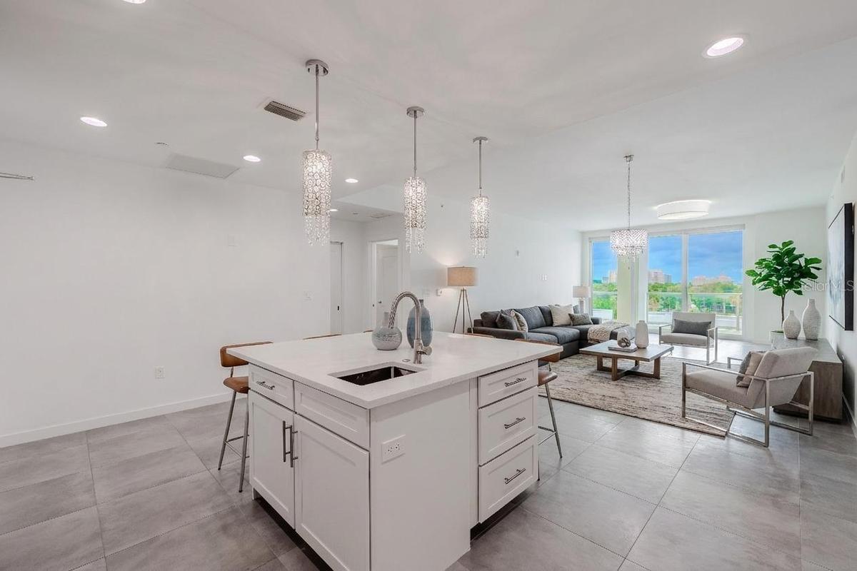 From the kitchen, enjoy an open-concept view that seamlessly connects the dining and living areas. Sleek tile flooring and designer lighting create a