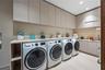 Large dedicated laundry room with dual washer and dryer sets, full-height flat-panel upper cabinetry, stone countertop, utility sink, light wood floor