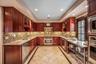 Kitchen with reddish brown cabinets, glass insert cabinets, inlaid floor details, light stone counters, and a raised ceiling