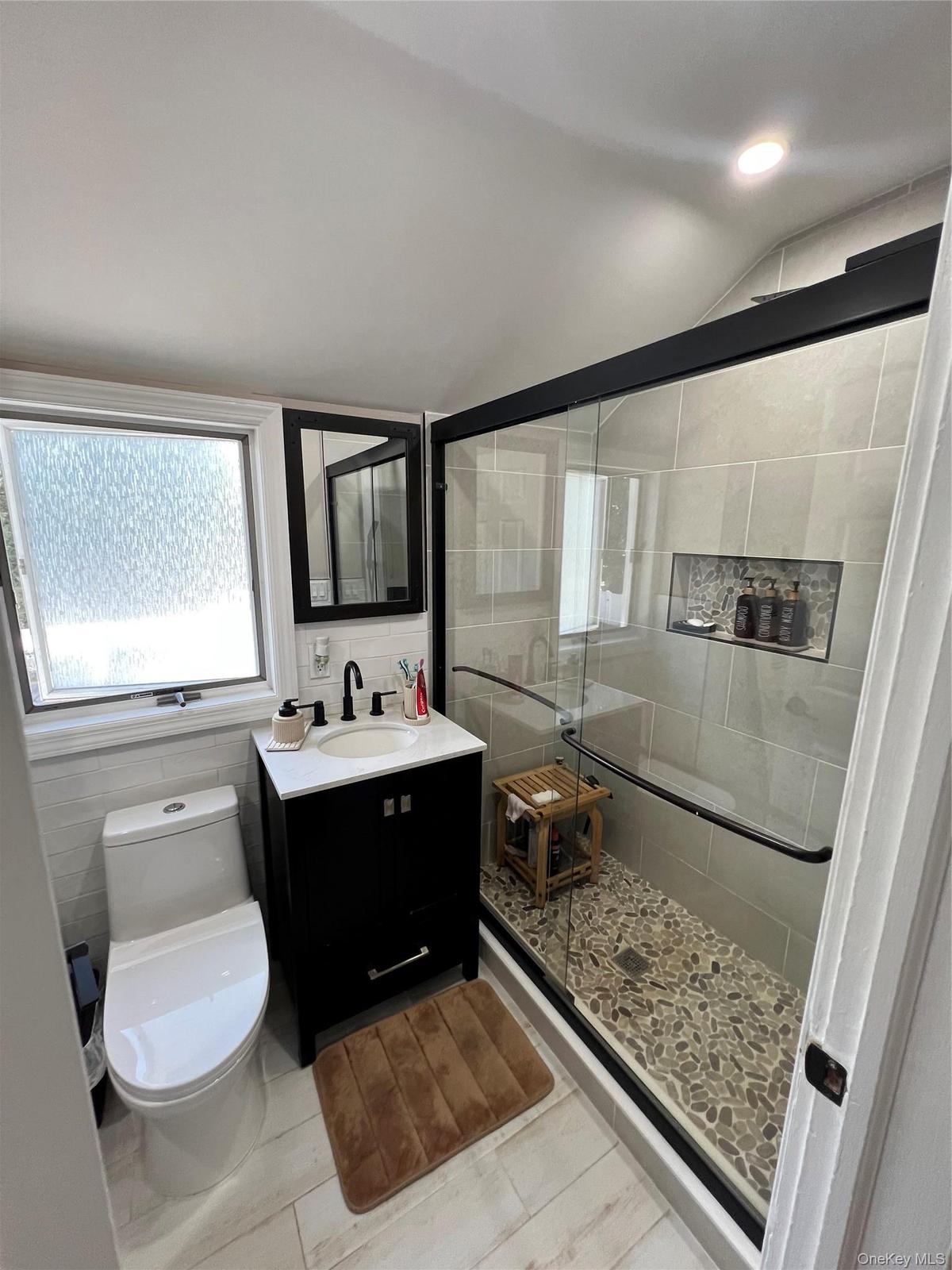 Walk-in shower with pebble tile flooring and glass enclosure