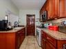 Galley kitchen featuring wood cabinetry, solid surface countertops, tile flooring, a tile backsplash, and a built-in microwave