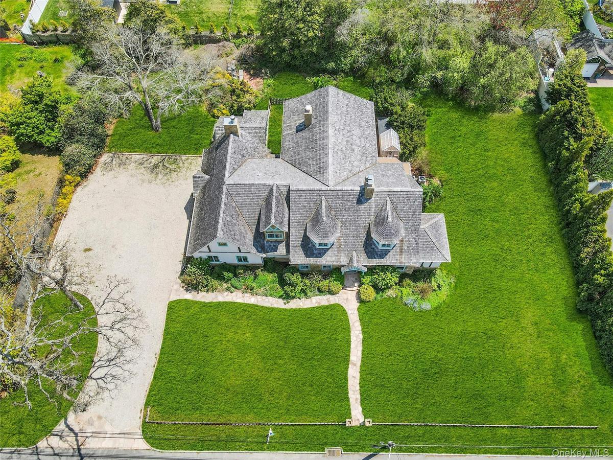 Exterior featuring a multi-gabled roof, three turret-style dormers, extensive lawn, a stone pathway, and a gravel driveway