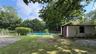 Fenced swimming pool, detached stucco structure, mature trees, green lawn, natural rock elements