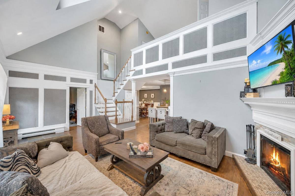 Two-story living area featuring a vaulted ceiling with skylights, hardwood-finish flooring, a fireplace with a white mantel, and an open staircase wit