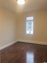 Bright, light-filled bedroom featuring gleaming wood-finish flooring, fresh neutral walls, and a transom window with natural light