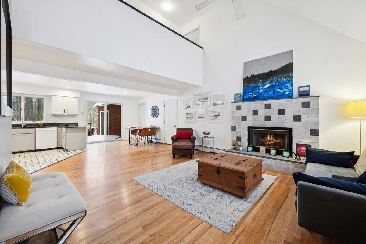Living room featuring a tiled fireplace, high vaulted ceiling, light hardwood / wood-style floors, and a baseboard heating unit