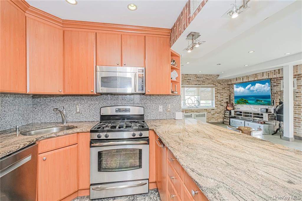 Kitchen featuring appliances with stainless steel finishes, open shelves, light stone counters, a peninsula, and recessed lighting