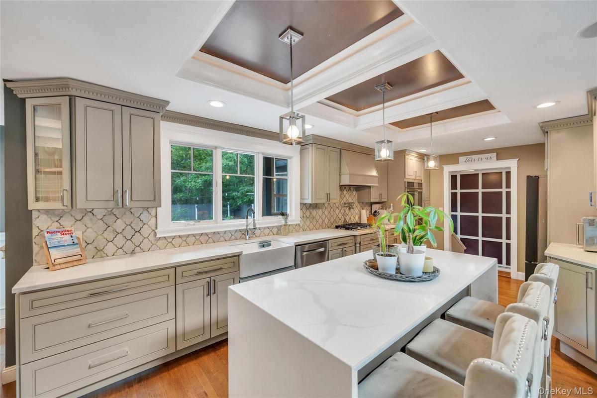 Expansive kitchen featuring a large central island with seating, a deep farmhouse-style sink, a patterned tile backsplash, and recessed and pendant li