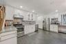 Kitchen with stainless steel appliances, glass fronted cabinets, white cabinets, dark wood-type flooring, and recessed lighting
