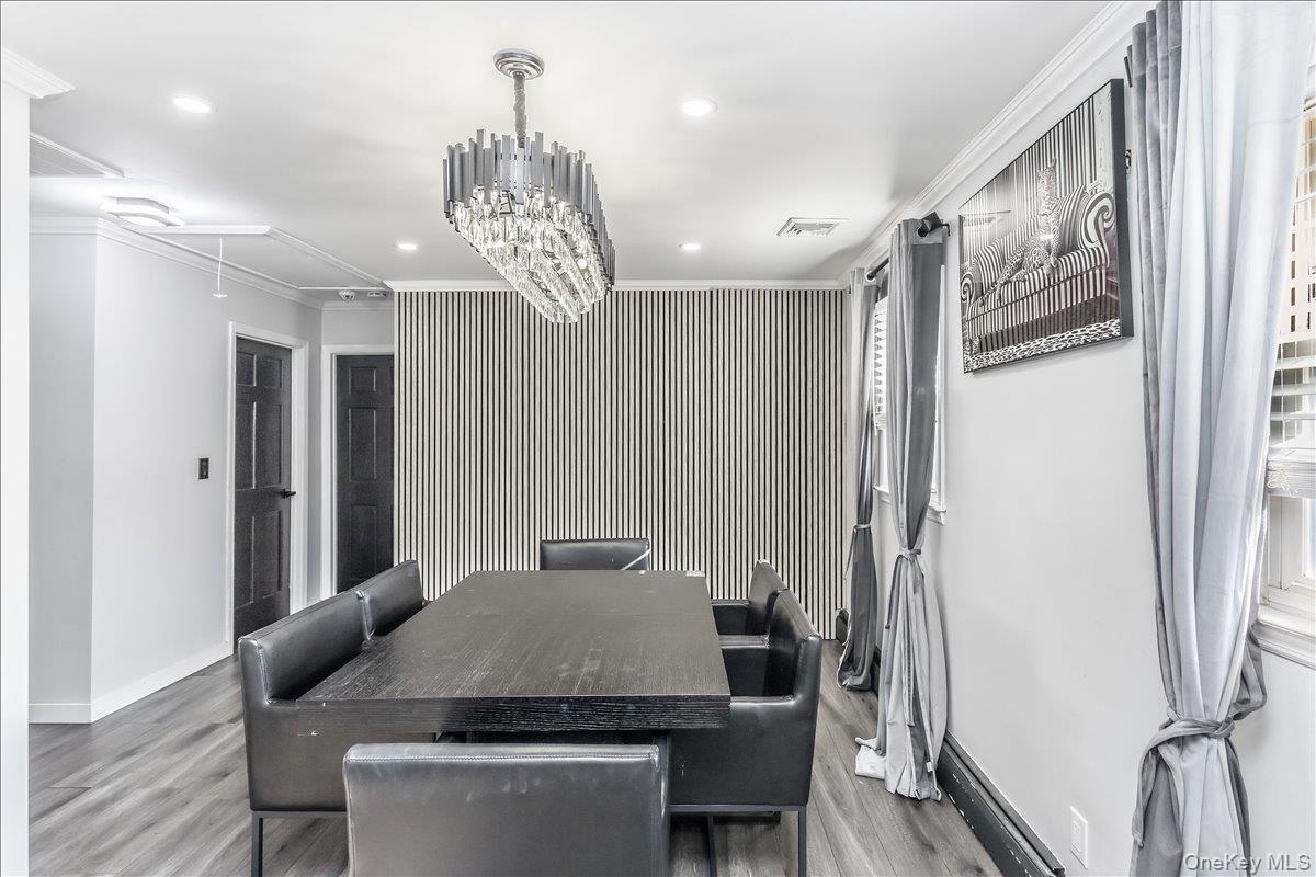 Dining space featuring wood-finish flooring, a contemporary crystal chandelier, a striped accent wall, and two paneled doors with dark finishes