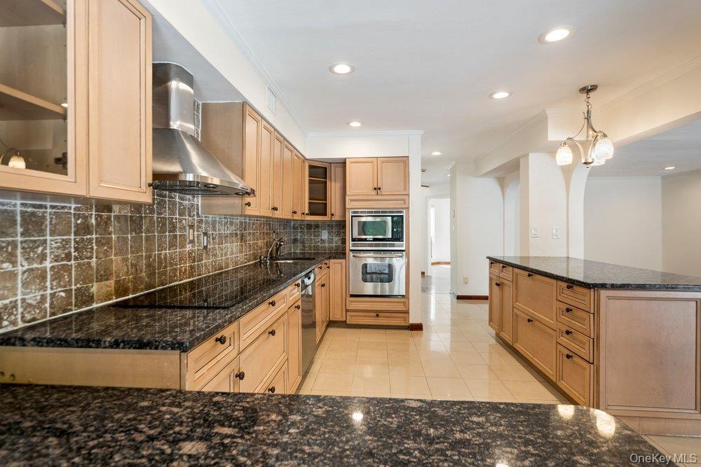 Kitchen featuring light wood-finish cabinetry, dark speckled countertops, and an integrated wall oven with a microwave