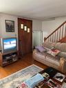 Comfortable living room featuring hardwood flooring, a striped upholstered sofa with rolled arms, wooden staircase with metal railings, and a wood-fin