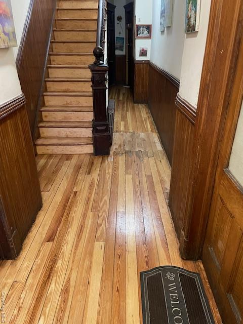 Corridor with light wood finished floors, a wainscoted wall, stairway, and wooden walls