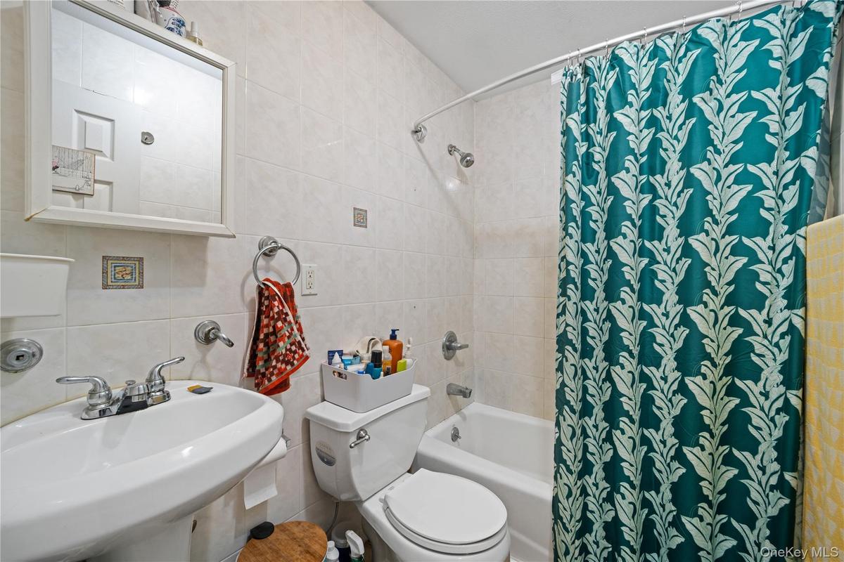 Bathroom featuring pedestal sink, chrome faucet, wall-mounted mirror, white ceramic tile, and a shower/tub combination
