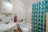 Bathroom featuring pedestal sink, chrome faucet, wall-mounted mirror, white ceramic tile, and a shower/tub combination