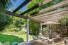 Expansive backyard featuring a wood deck with a pergola, a manicured lawn, and mature trees