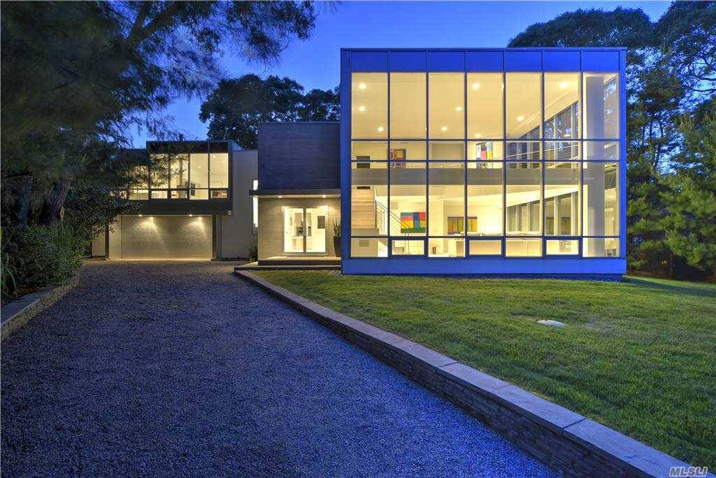 This minimalist treasure, with its aluminum and glass exterior in a deep grey hue, sits dramatically elevated at the end of a meandering driveway.