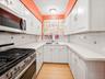 Galley kitchen featuring white cabinetry, light countertops, tile backsplash, stainless steel range, and an integrated microwave