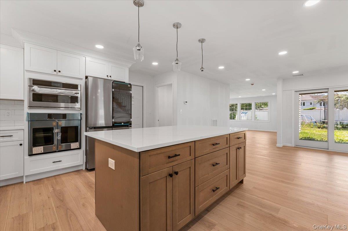 Contemporary kitchen featuring a large central island with a light-toned wood finish, white countertops, built-in stainless steel appliances, and whit