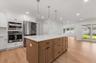 Contemporary kitchen featuring a large central island with a light-toned wood finish, white countertops, built-in stainless steel appliances, and whit