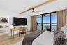 Second bedroom configured as a guest room and home-office setup with a private balcony, bay view, and motorized blinds.