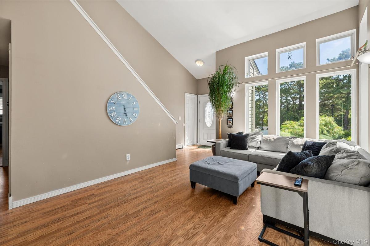 Vaulted ceiling living area featuring wood-finish flooring, a wall of multiple windows, and a white paneled front door