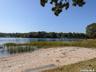 Sandy waterfront featuring a wooden bench, marsh grass, and a distant pier
