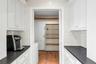 Galley-style utility space featuring upper and lower white cabinetry, dark stone countertops and a handmade decorative tiled backsplash