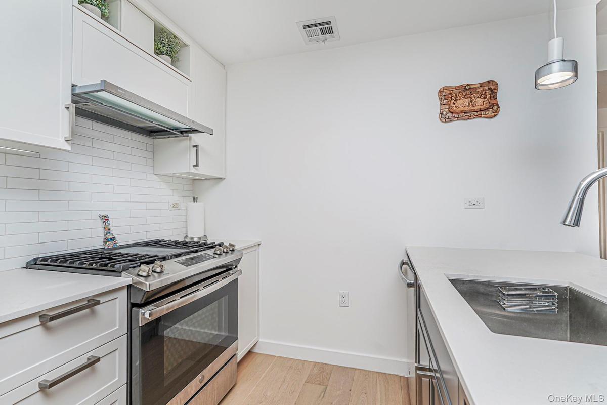 Kitchen with stainless steel appliances, light wood-type flooring, tasteful backsplash, and white cabinets