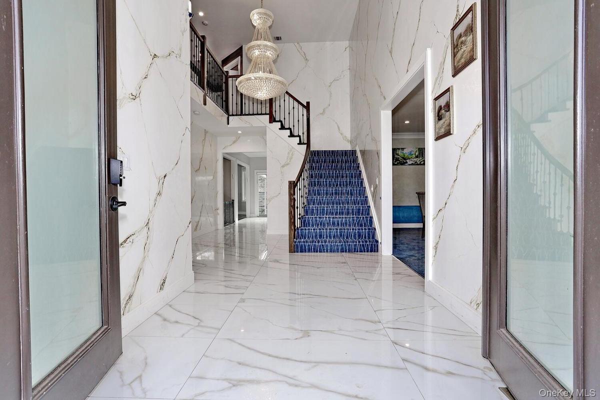 Foyer entrance with stairway, a chandelier, marble tiled flooring, a high ceiling, and stone wall