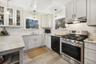 Kitchen with gas stove, glass insert cabinets, under cabinet range hood, hanging light fixtures, and black dishwasher
