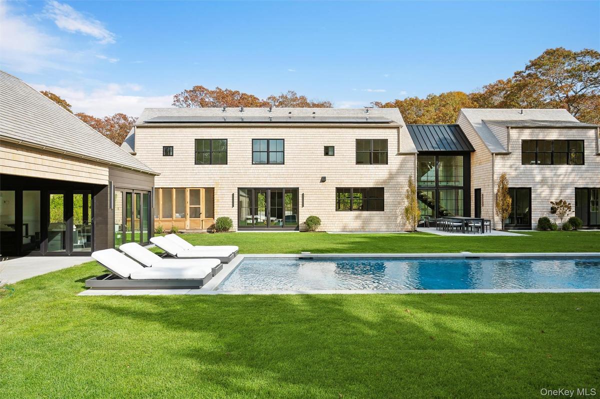 Rear view of property featuring a sunroom, a patio area, and a lawn