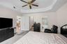 Carpeted bedroom featuring a tray ceiling, a chandelier, a ceiling fan, and ensuite bathroom
