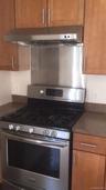 Kitchen with gas stove, under cabinet range hood, dark countertops, and brown cabinets