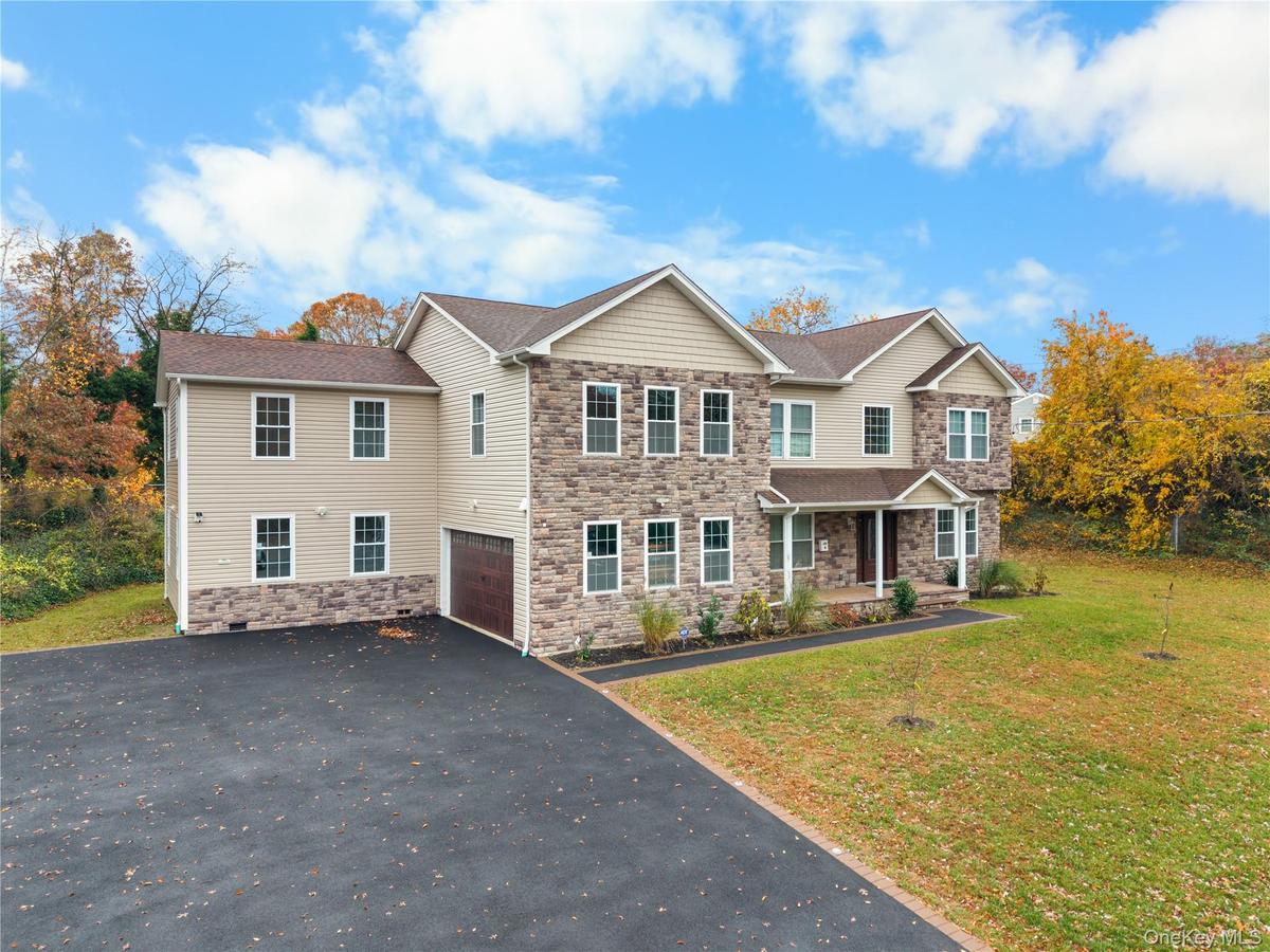 View of front of property featuring covered porch, asphalt driveway, stone siding, a garage, and a front yard