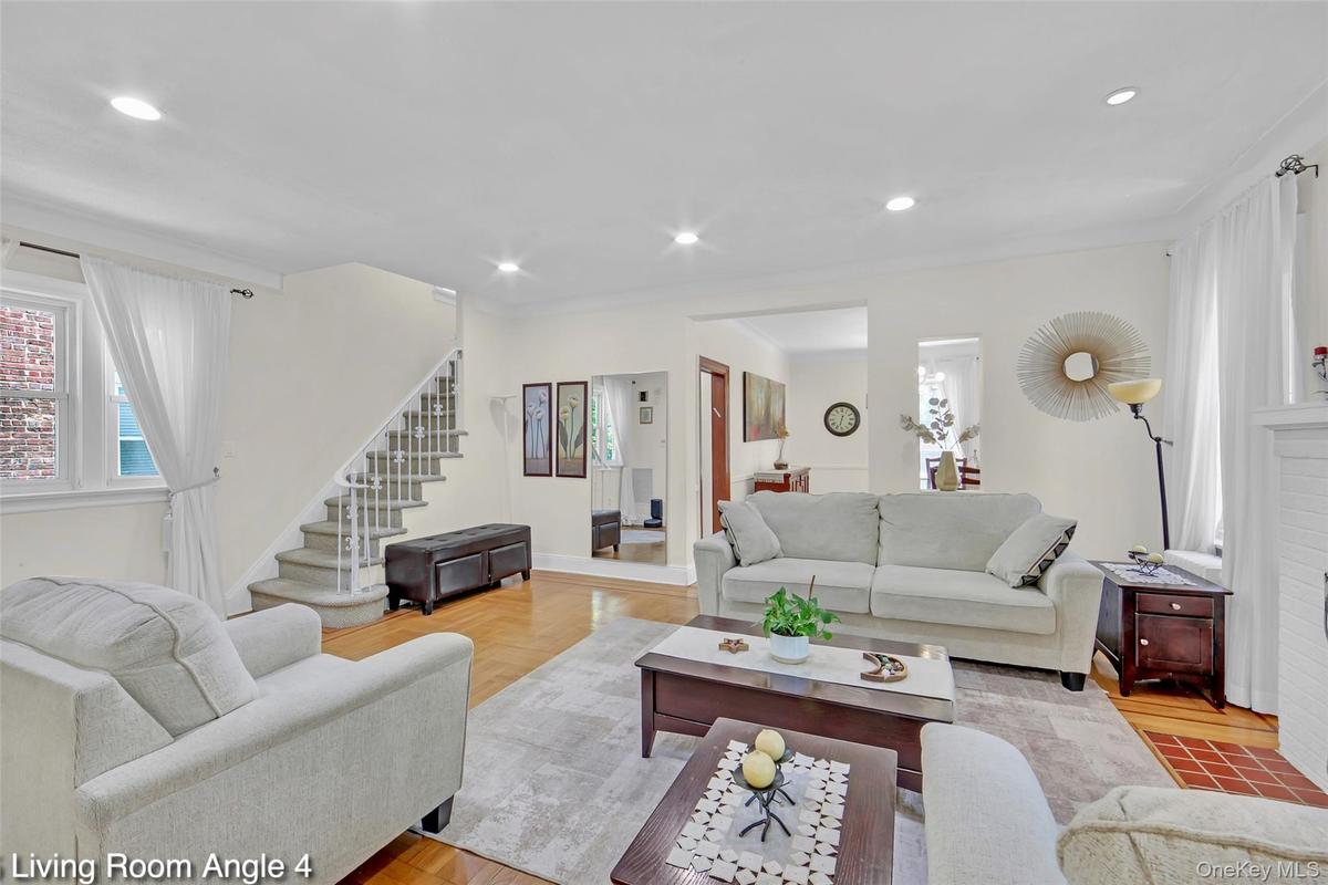 Inviting living room featuring hardwood flooring, recessed lighting, and a prominent staircase with white balusters