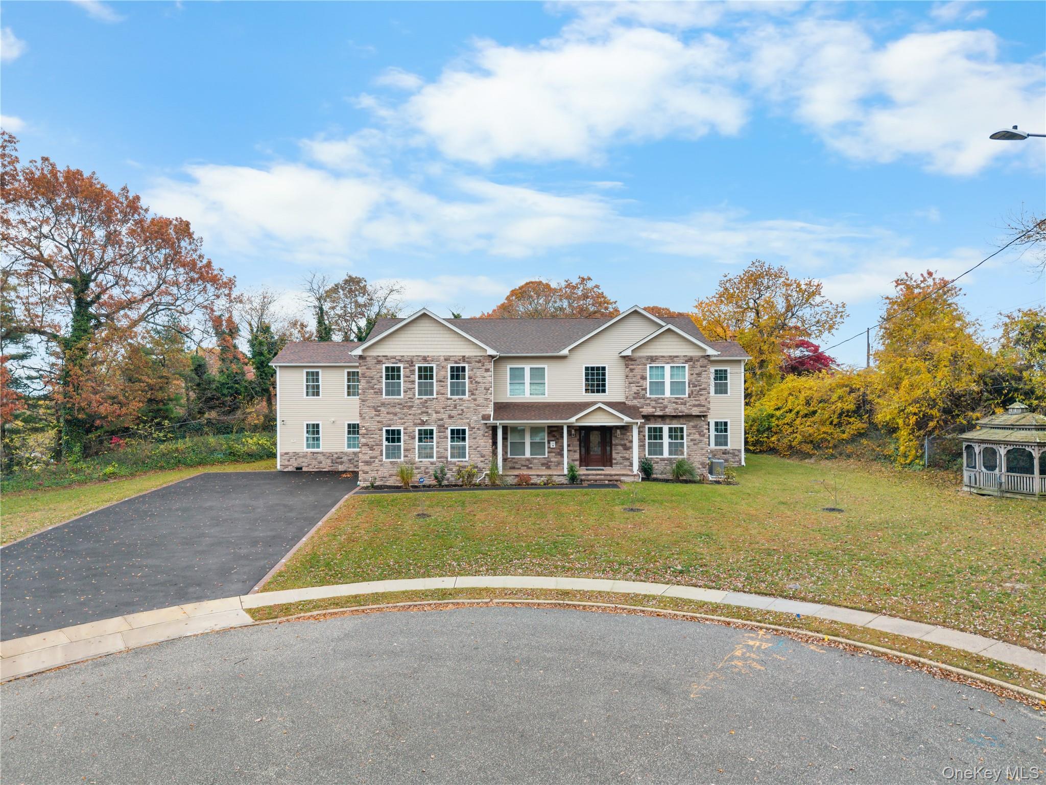 Traditional home with a porch, asphalt driveway, stone siding, and a front lawn