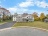 Traditional home with a porch, asphalt driveway, stone siding, and a front lawn