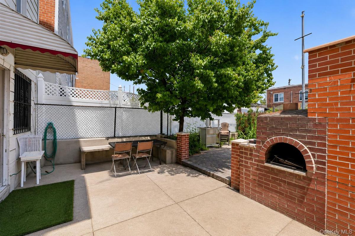 Outdoor patio featuring a built-in brick oven, concrete slab flooring, and a privacy fence with lattice detailing