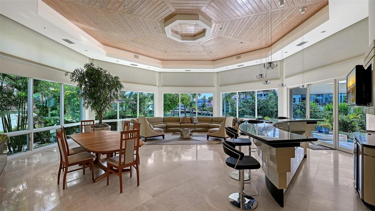 Vaulted great room for dining and entertaining with floor-to-ceiling windows, travertine floors, and a wood-paneled ceiling