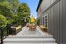 Expansive outdoor deck featuring wood-finish flooring, dark board-and-batten siding, black railings, and a mature tree canopy backdrop
