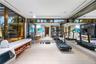 Full private gym and wellness suite with treadmills, kettlebells, yoga mats, massage table, full-wall mirror, wall-mounted TV, light wood floors, cler