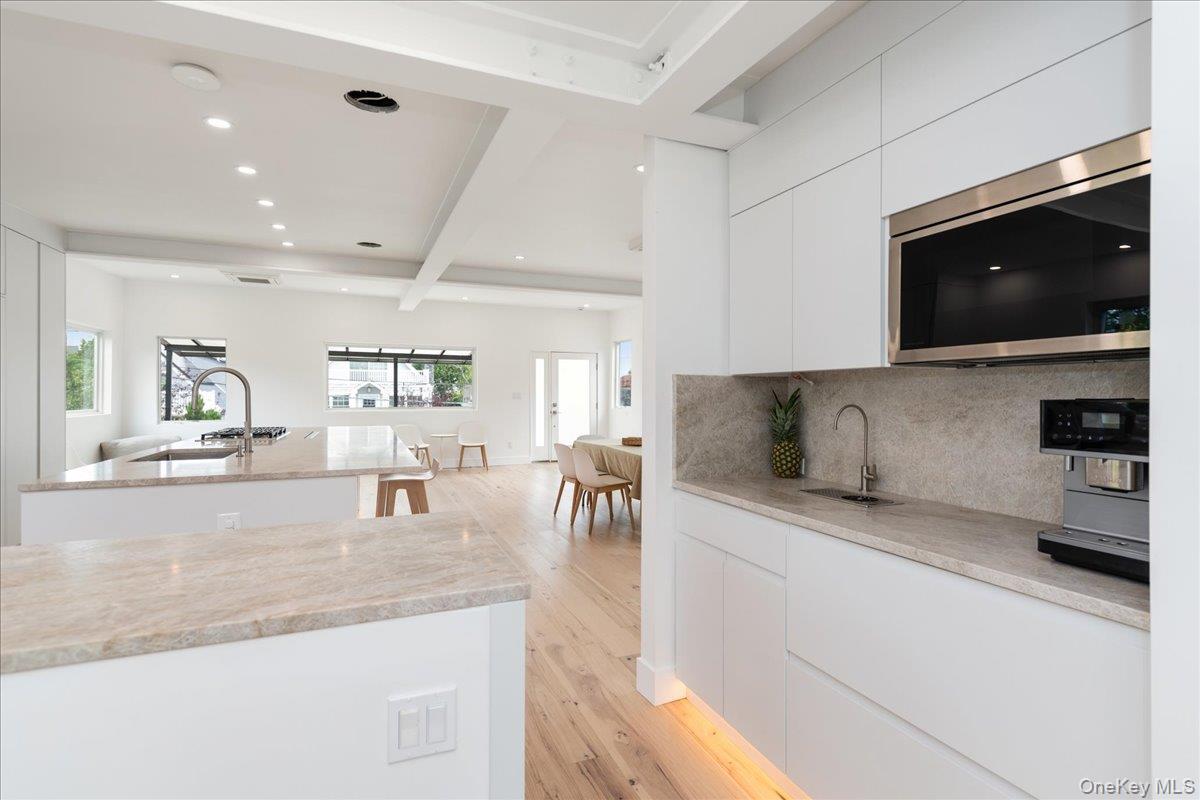 Kitchen featuring modern cabinets, stainless steel microwave, beam ceiling, light wood-type flooring, and a kitchen island with sink