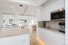 Kitchen featuring modern cabinets, stainless steel microwave, beam ceiling, light wood-type flooring, and a kitchen island with sink