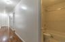 Hallway with wood-finish flooring leading to a full bathroom featuring a white tub, shower with a chrome fixture, and neutral-toned wall tiles