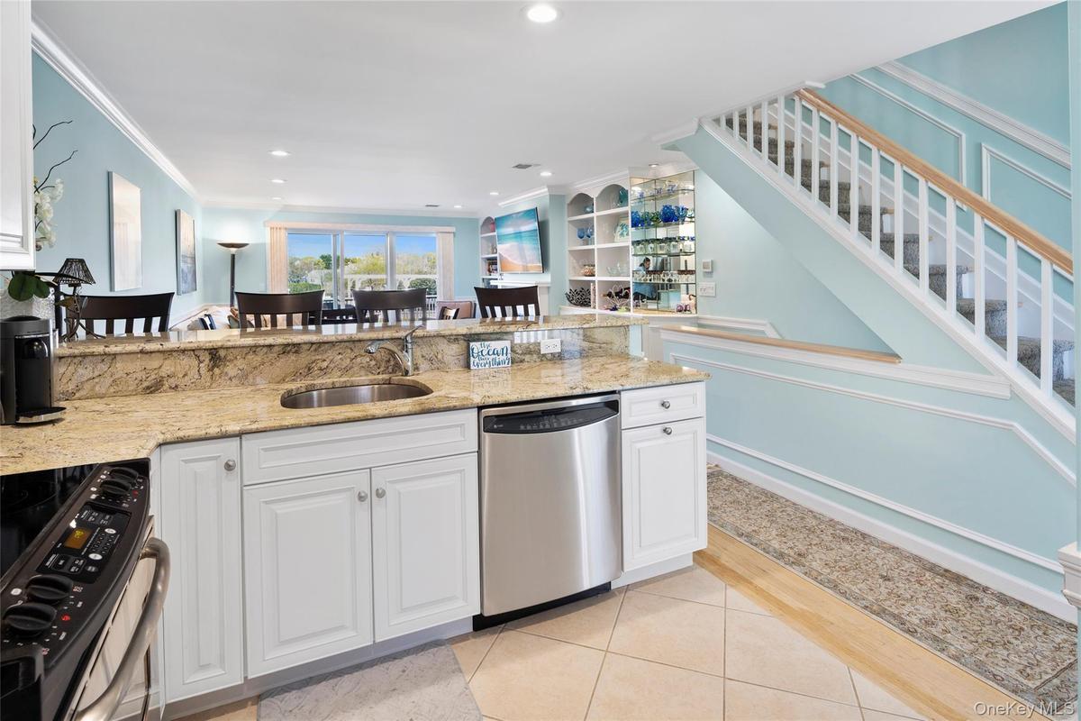 Kitchen featuring light stone counters, light tile patterned floors, a sink, crown molding, and appliances with stainless steel finishes