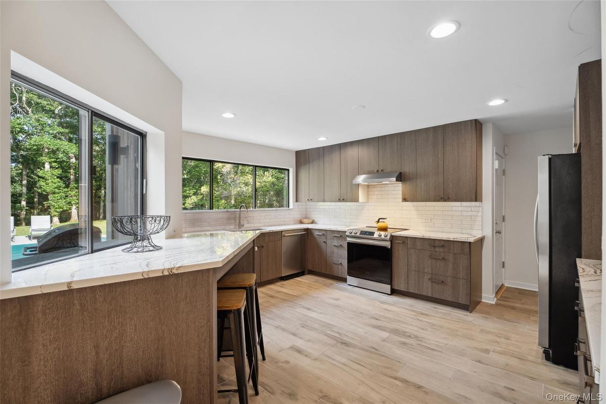 Kitchen featuring light stone counters, stainless steel appliances, tasteful backsplash, modern cabinets, and light wood-type flooring