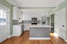 Kitchen featuring light stone countertops, white cabinetry, stainless steel appliances, ornamental molding, and light wood finished floors